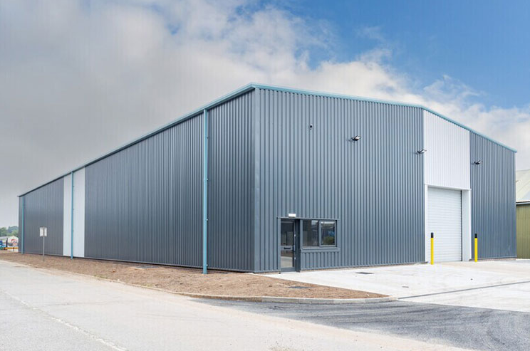 The exterior of a large grey warehouse, featuring a white roll-up door, an entrance way and a central window.